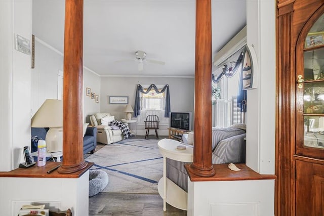 interior space featuring ceiling fan, decorative columns, ornamental molding, and wood finished floors