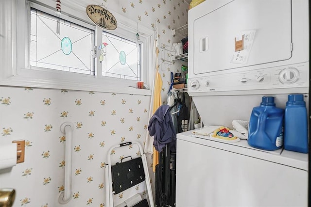 clothes washing area with wallpapered walls, stacked washing maching and dryer, and laundry area