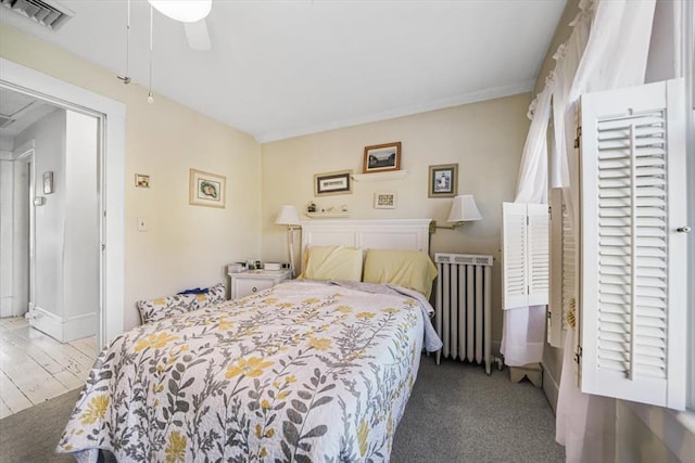 bedroom with a ceiling fan, visible vents, radiator heating unit, and wood finished floors