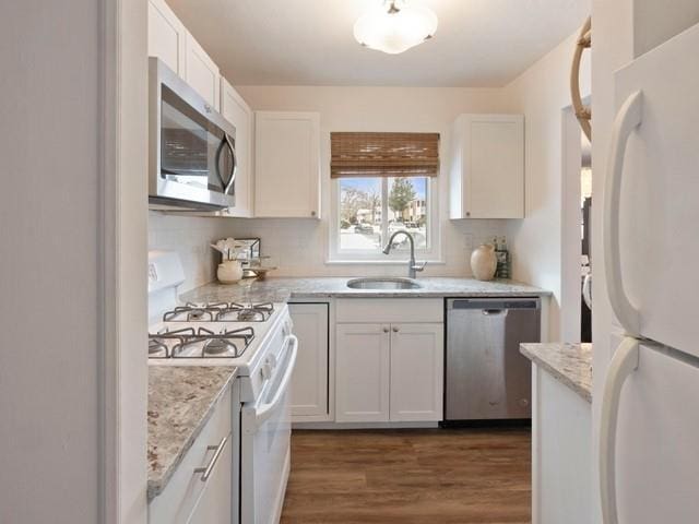 kitchen featuring dark wood-style floors, appliances with stainless steel finishes, light stone countertops, white cabinetry, and a sink