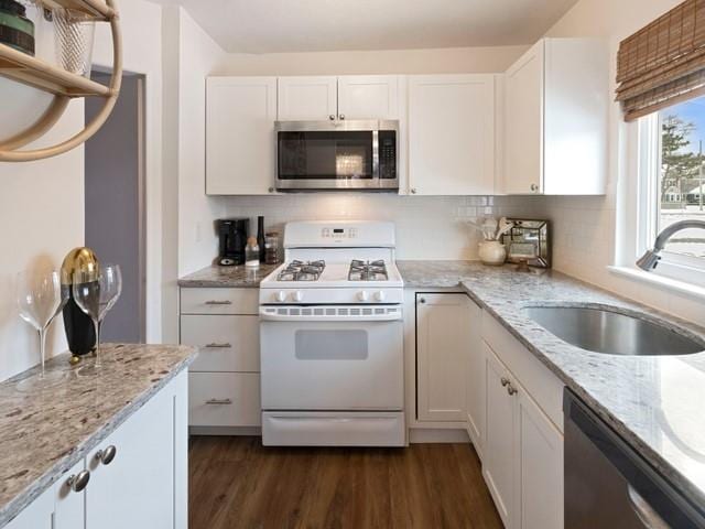 kitchen featuring open shelves, appliances with stainless steel finishes, white cabinetry, a sink, and light stone countertops