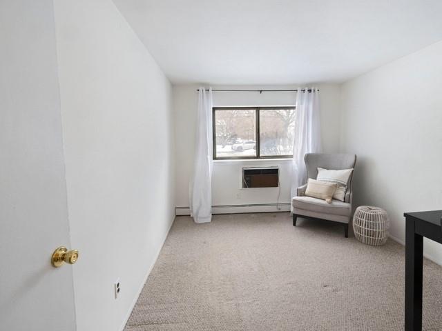 sitting room with a baseboard radiator, an AC wall unit, and light carpet