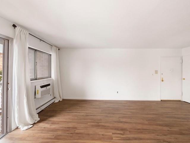 empty room with baseboard heating, wood finished floors, and a wall mounted air conditioner