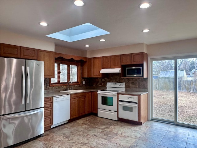 kitchen with under cabinet range hood, stainless steel appliances, a skylight, a sink, and decorative backsplash