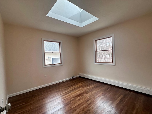 empty room with a healthy amount of sunlight, a skylight, a baseboard radiator, and dark wood-style floors