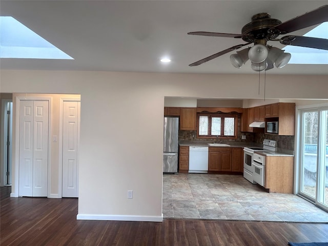 kitchen featuring decorative backsplash, brown cabinetry, stainless steel appliances, under cabinet range hood, and a sink