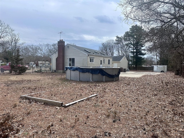 view of side of home with a covered pool, a chimney, and fence