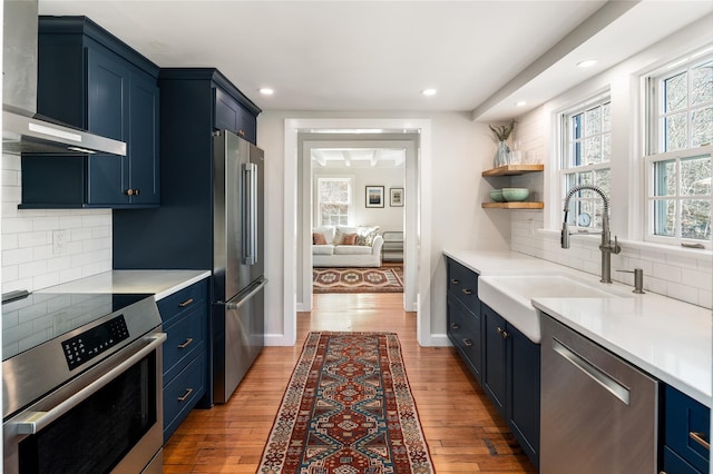 kitchen with appliances with stainless steel finishes, blue cabinetry, and wall chimney exhaust hood