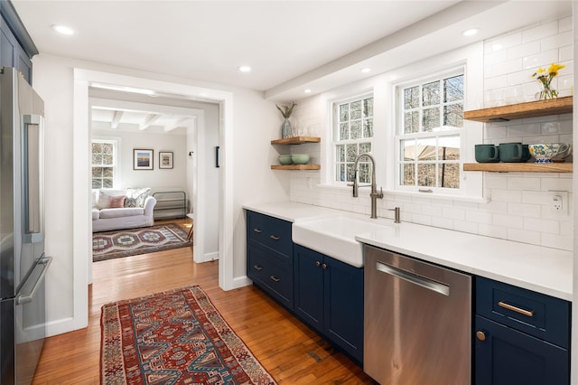 kitchen featuring a sink, wood finished floors, appliances with stainless steel finishes, blue cabinetry, and open shelves