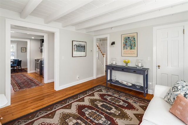 interior space featuring wood finished floors, beamed ceiling, baseboards, and stairs