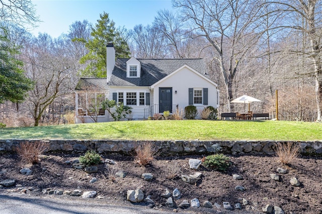 cape cod-style house featuring a shingled roof, a chimney, and a front yard