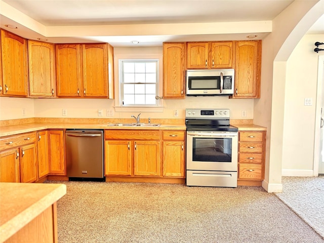 kitchen featuring stainless steel appliances, a sink, baseboards, light countertops, and brown cabinetry