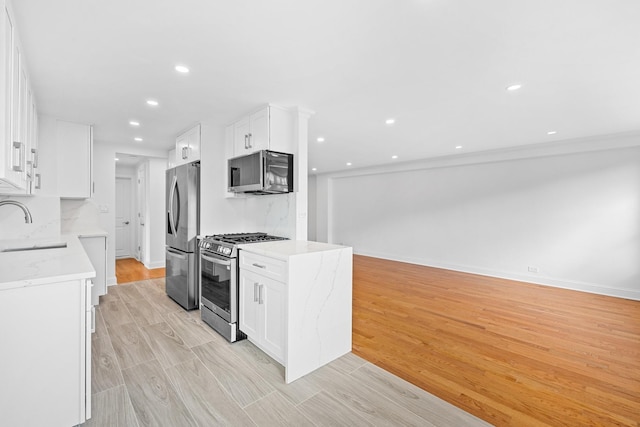 kitchen with light stone counters, appliances with stainless steel finishes, white cabinets, and a sink