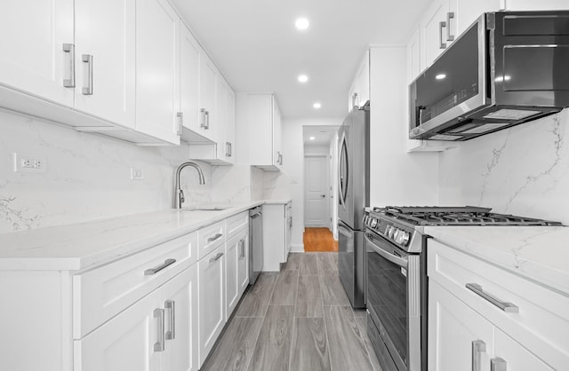 kitchen featuring decorative backsplash, light stone counters, stainless steel appliances, white cabinetry, and a sink