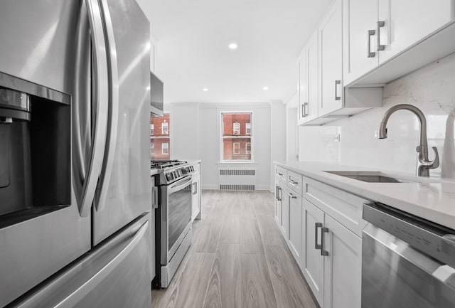 kitchen with appliances with stainless steel finishes, white cabinets, light countertops, and radiator heating unit