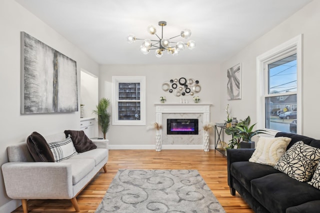 living area featuring light wood-style flooring, a fireplace, baseboards, and a notable chandelier