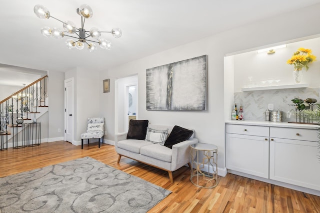 living room featuring light wood-type flooring, an inviting chandelier, stairs, and baseboards