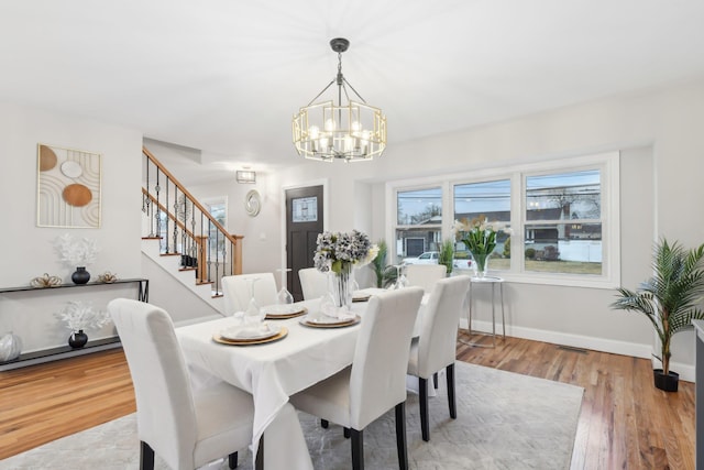 dining area featuring an inviting chandelier, baseboards, stairway, and wood finished floors