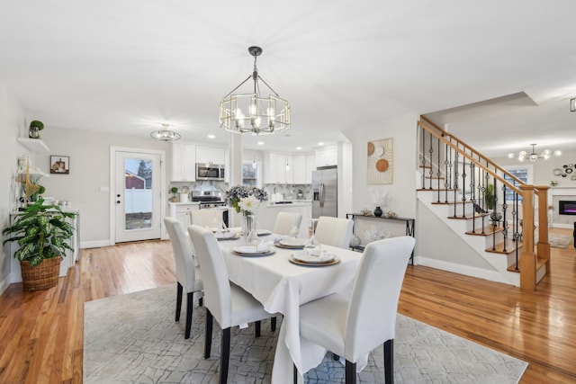 dining room with stairs, light wood-style floors, baseboards, and an inviting chandelier