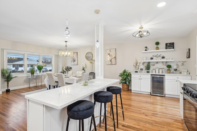 kitchen featuring beverage cooler, a kitchen breakfast bar, an inviting chandelier, light wood-type flooring, and stainless steel range with electric stovetop