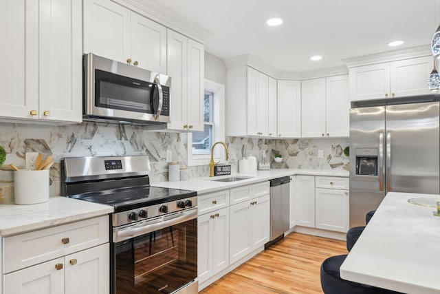 kitchen featuring light wood finished floors, stainless steel appliances, tasteful backsplash, white cabinetry, and a sink