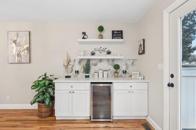 bar with beverage cooler, visible vents, baseboards, a bar, and light wood-style floors