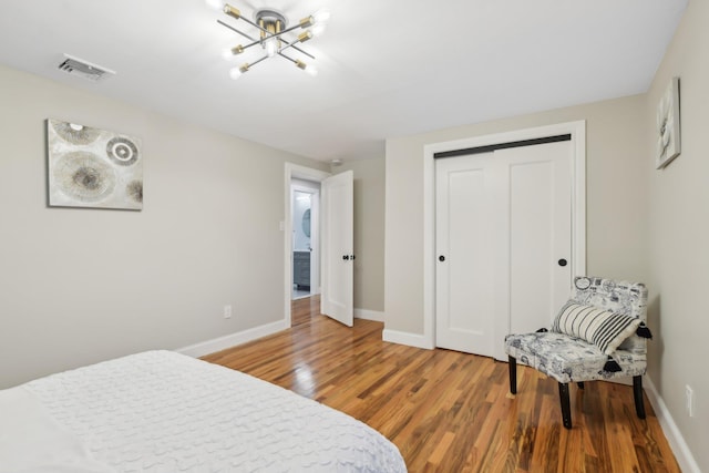 bedroom with a closet, visible vents, wood finished floors, a chandelier, and baseboards