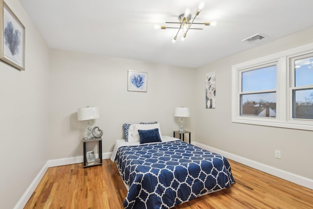 bedroom featuring an inviting chandelier, wood finished floors, visible vents, and baseboards