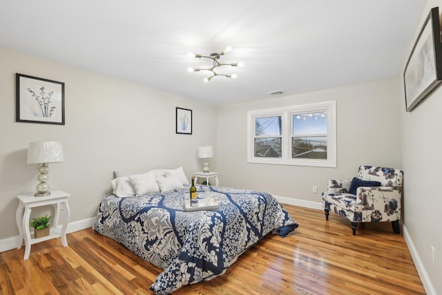 bedroom featuring an inviting chandelier, wood finished floors, visible vents, and baseboards