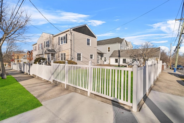 view of side of home featuring a fenced front yard, a residential view, a lawn, and board and batten siding