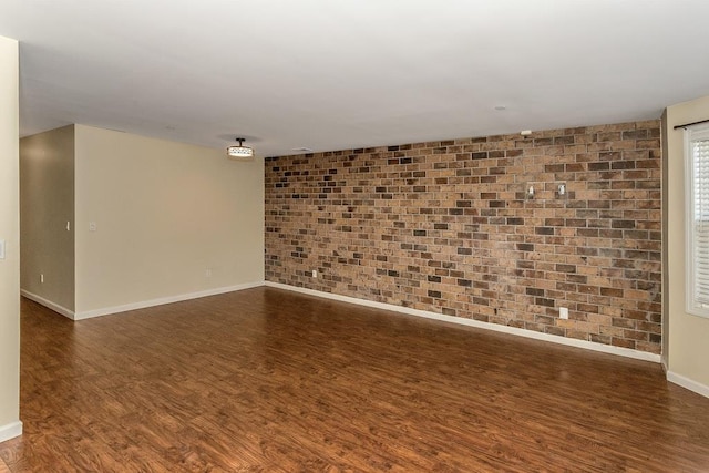 spare room featuring dark wood-style flooring, baseboards, and brick wall