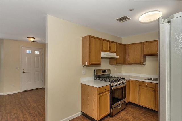 kitchen featuring stainless steel gas range oven, under cabinet range hood, dark wood-style flooring, light countertops, and brown cabinetry