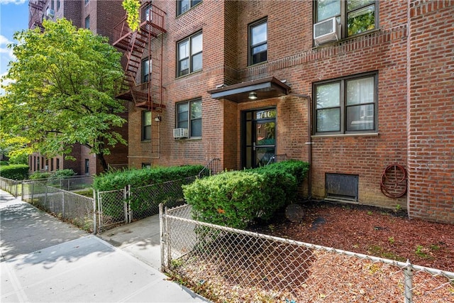 view of exterior entry with fence, cooling unit, and brick siding