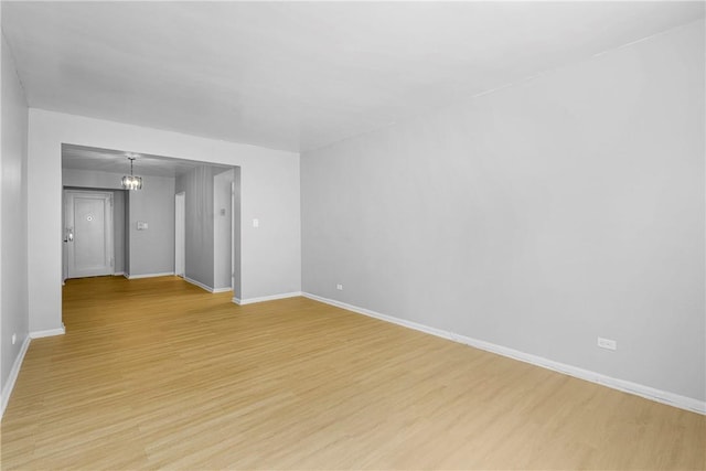 empty room featuring light wood-type flooring, baseboards, and a notable chandelier