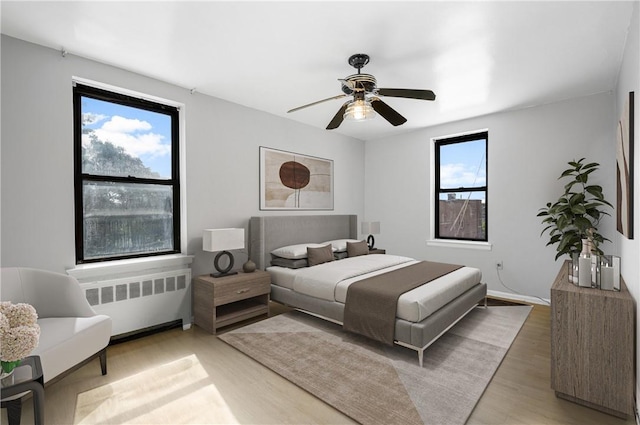 bedroom featuring a ceiling fan, radiator heating unit, and wood finished floors