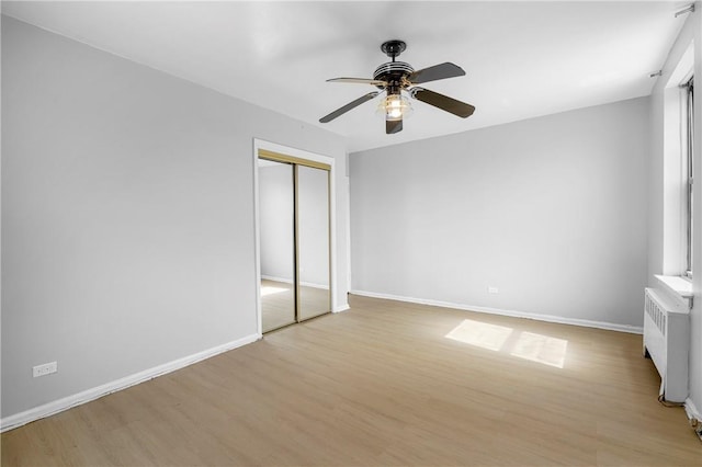 unfurnished bedroom featuring radiator, a closet, light wood-style floors, ceiling fan, and baseboards