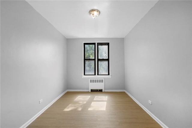 spare room with light wood-type flooring, radiator heating unit, and baseboards