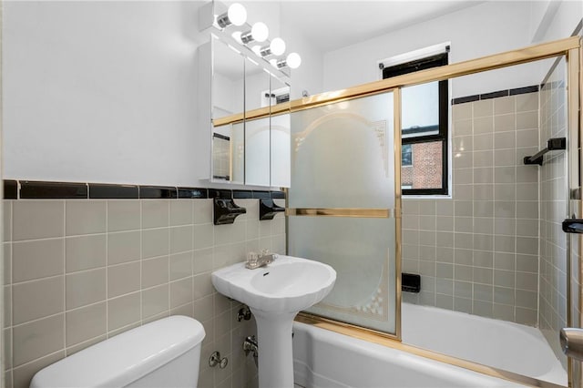 bathroom with shower / bath combination with glass door, wainscoting, toilet, and tile walls