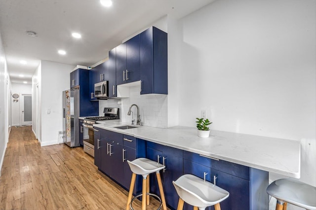 kitchen with blue cabinets, stainless steel appliances, a peninsula, a sink, and a kitchen bar