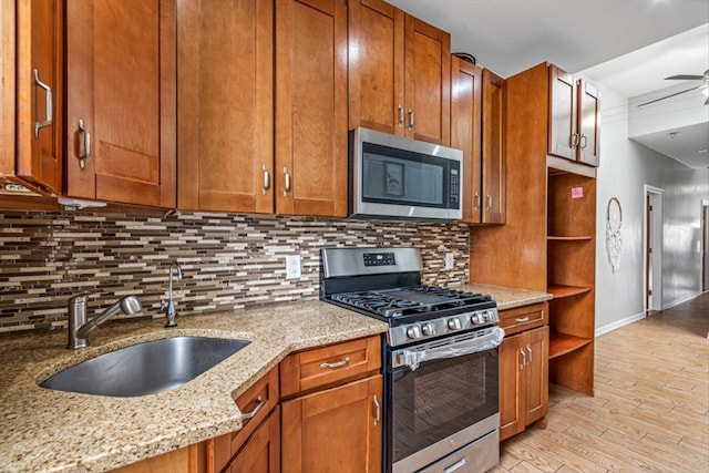 kitchen with light stone countertops, stainless steel appliances, a sink, decorative backsplash, and open shelves