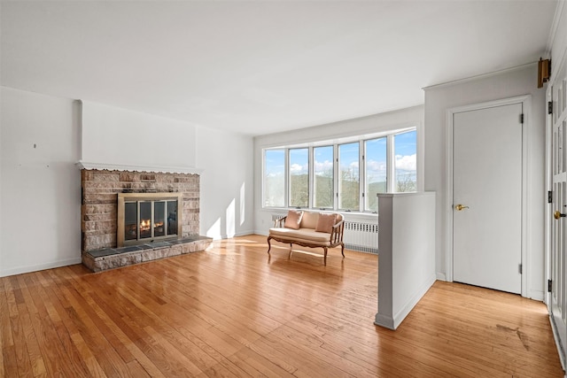 unfurnished living room featuring radiator, baseboards, a fireplace, and light wood finished floors