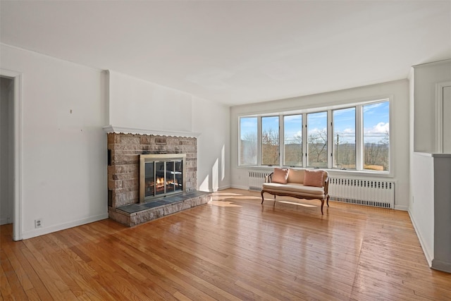 interior space featuring light wood-style floors, a glass covered fireplace, radiator, and baseboards