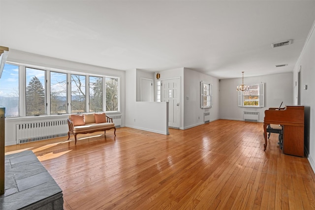 living room featuring a chandelier, light wood-type flooring, radiator, and a wealth of natural light