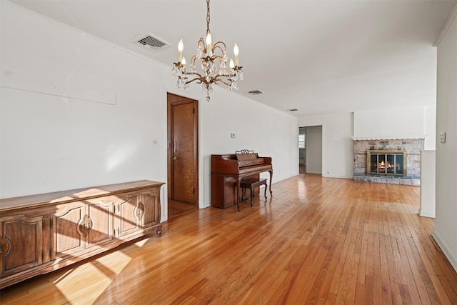 unfurnished living room with a stone fireplace, visible vents, light wood-style flooring, and an inviting chandelier