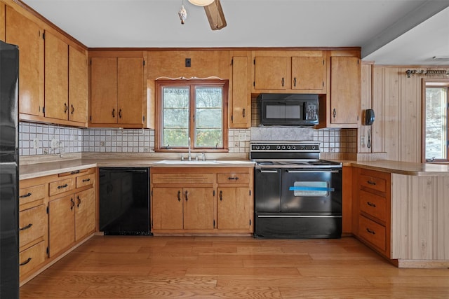 kitchen featuring light wood-style flooring, a sink, light countertops, black appliances, and tasteful backsplash