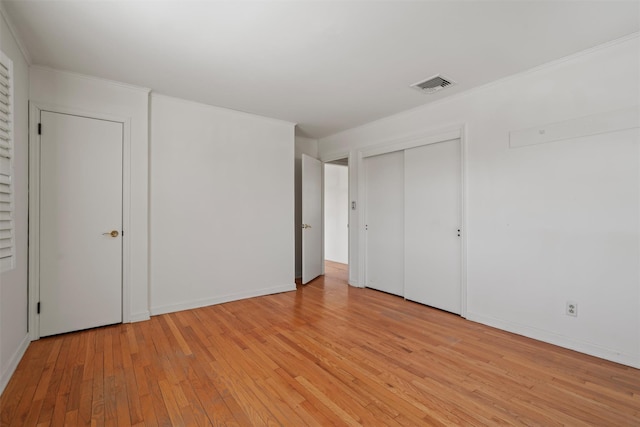 unfurnished bedroom with baseboards, visible vents, crown molding, light wood-type flooring, and a closet