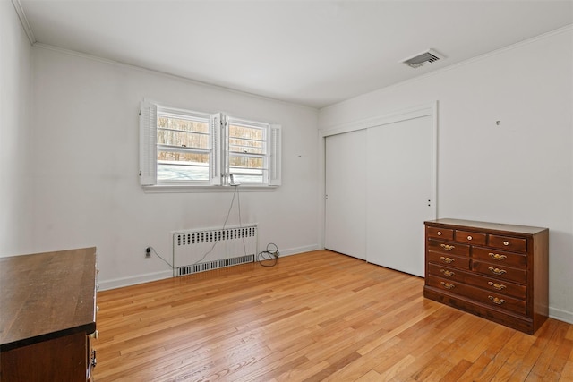 unfurnished bedroom featuring baseboards, radiator heating unit, ornamental molding, light wood-type flooring, and a closet