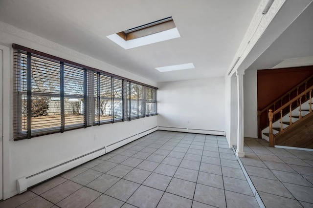 empty room featuring light tile patterned floors, baseboard heating, a skylight, and stairs