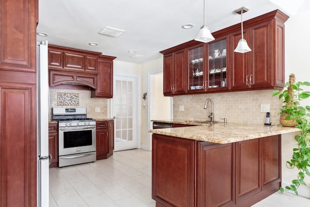 kitchen featuring a peninsula, stainless steel range with gas stovetop, a sink, glass insert cabinets, and pendant lighting