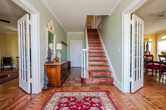 stairs with french doors, parquet floors, crown molding, a ceiling fan, and baseboards